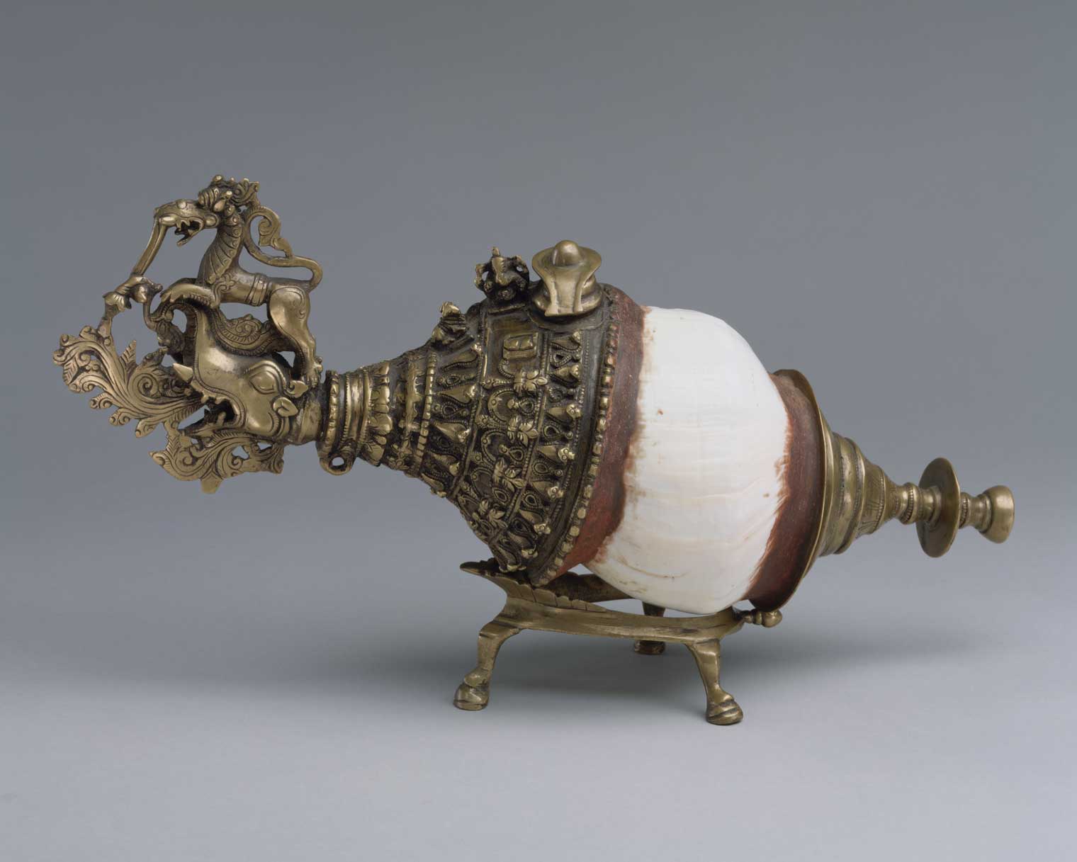 A conch shell with elaborate brass decoration on both sides and brass legs