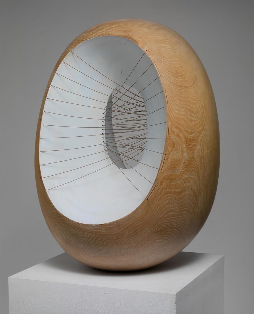 Wooden, oval sculpture with multiple strings crossing through the center.