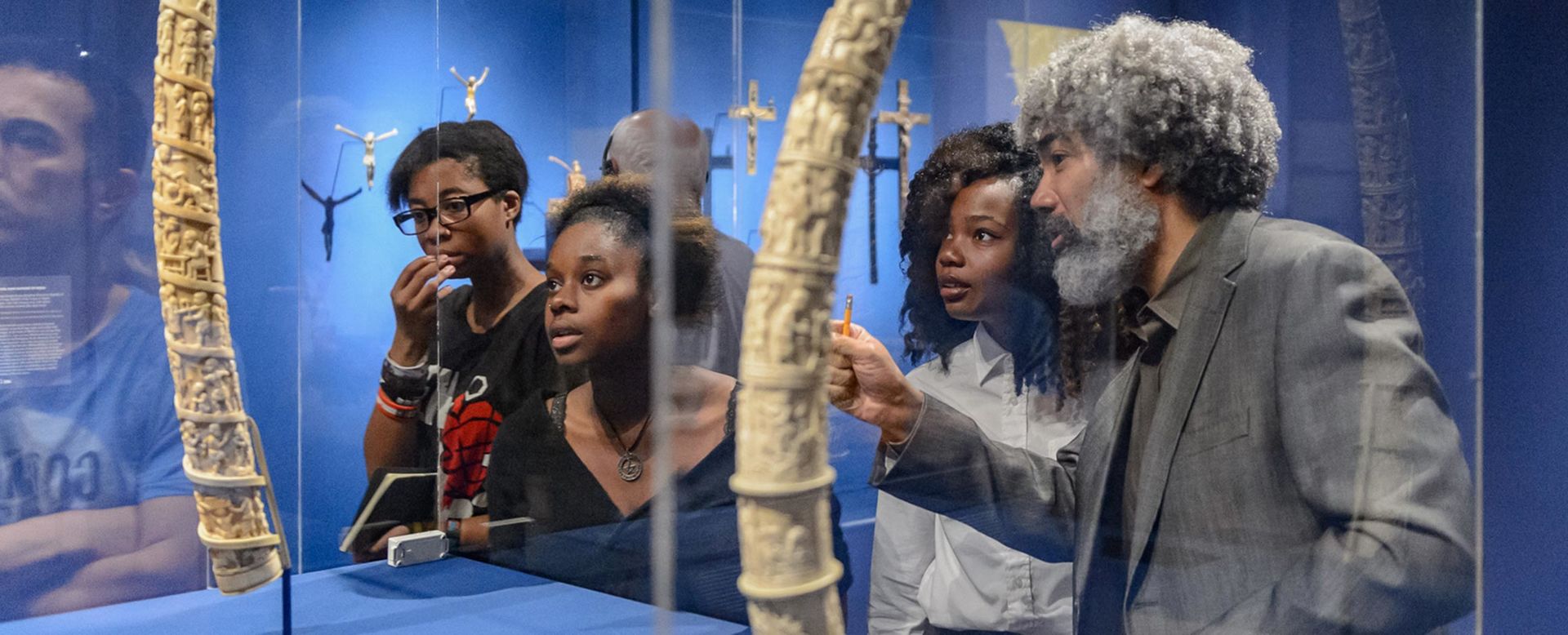 A teacher points to an ivory altar tusk to a group of students in a blue room