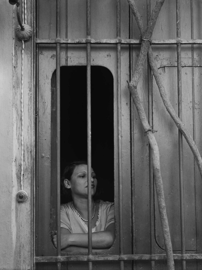A black-and-white photograph of a woman peering through bars