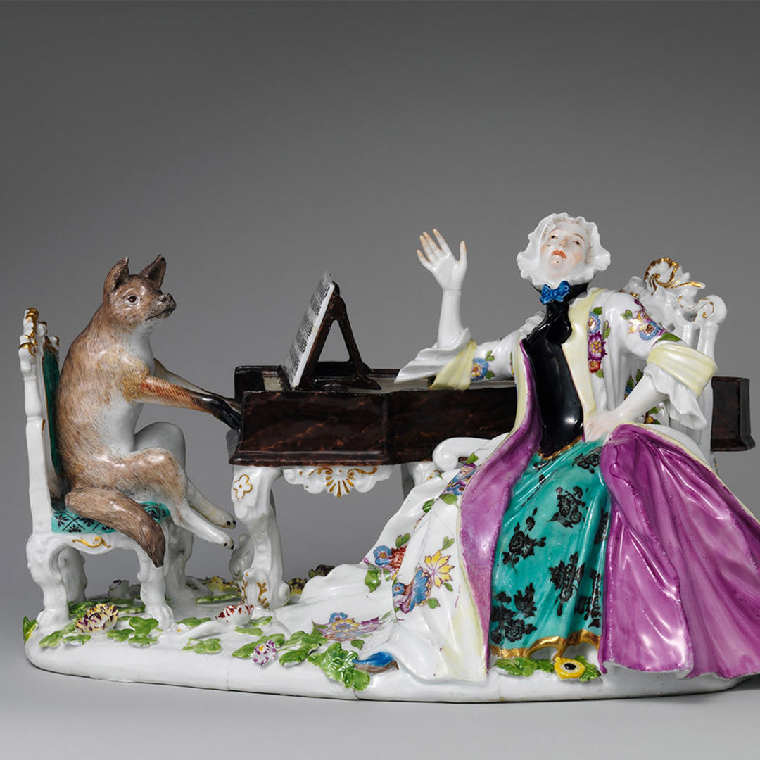 Sculpture of a fox sitting on a bench playing the piano while a regally dressed woman looks upwards