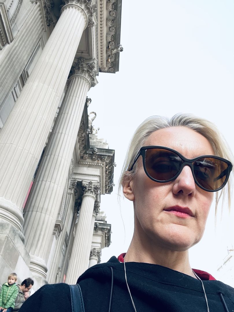 Photo of person wearing sunglasses outdoors against columns and grey sky.