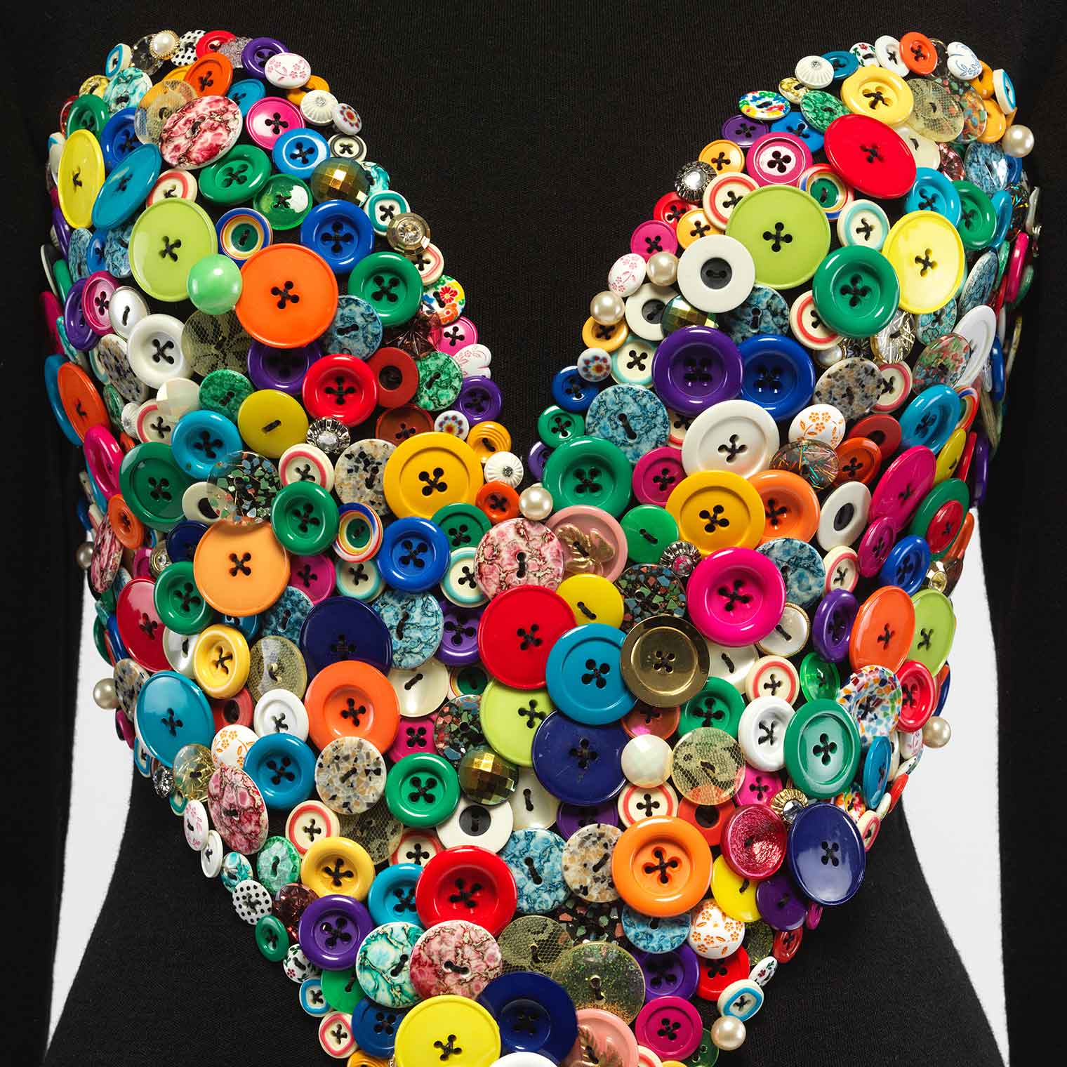 Detail of a black dress by Patrick Kelly with a large collection of colorful buttons in the shape of a heart on the bodice