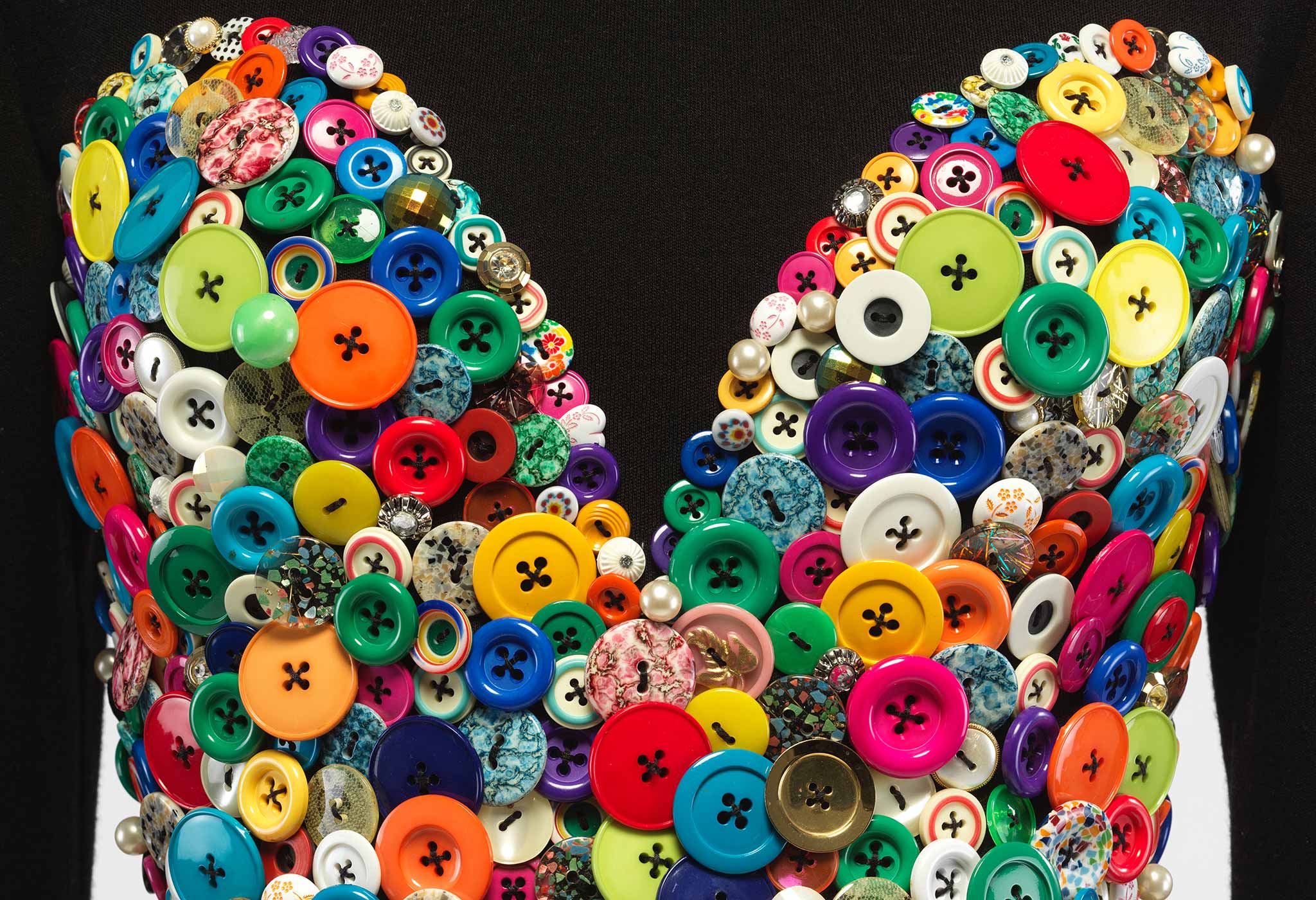 Detail of a black dress by Patrick Kelly with a large collection of colorful buttons in the shape of a heart on the bodice
