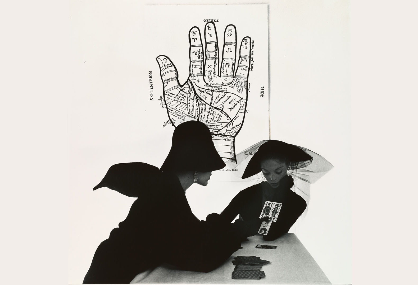 Irving Penn's "The Tarot Reader (Bridget Tichenor and Jean Patchett), New York" with two women in stylist black clothing reading tarot cards with a diagram of a hand behind them
