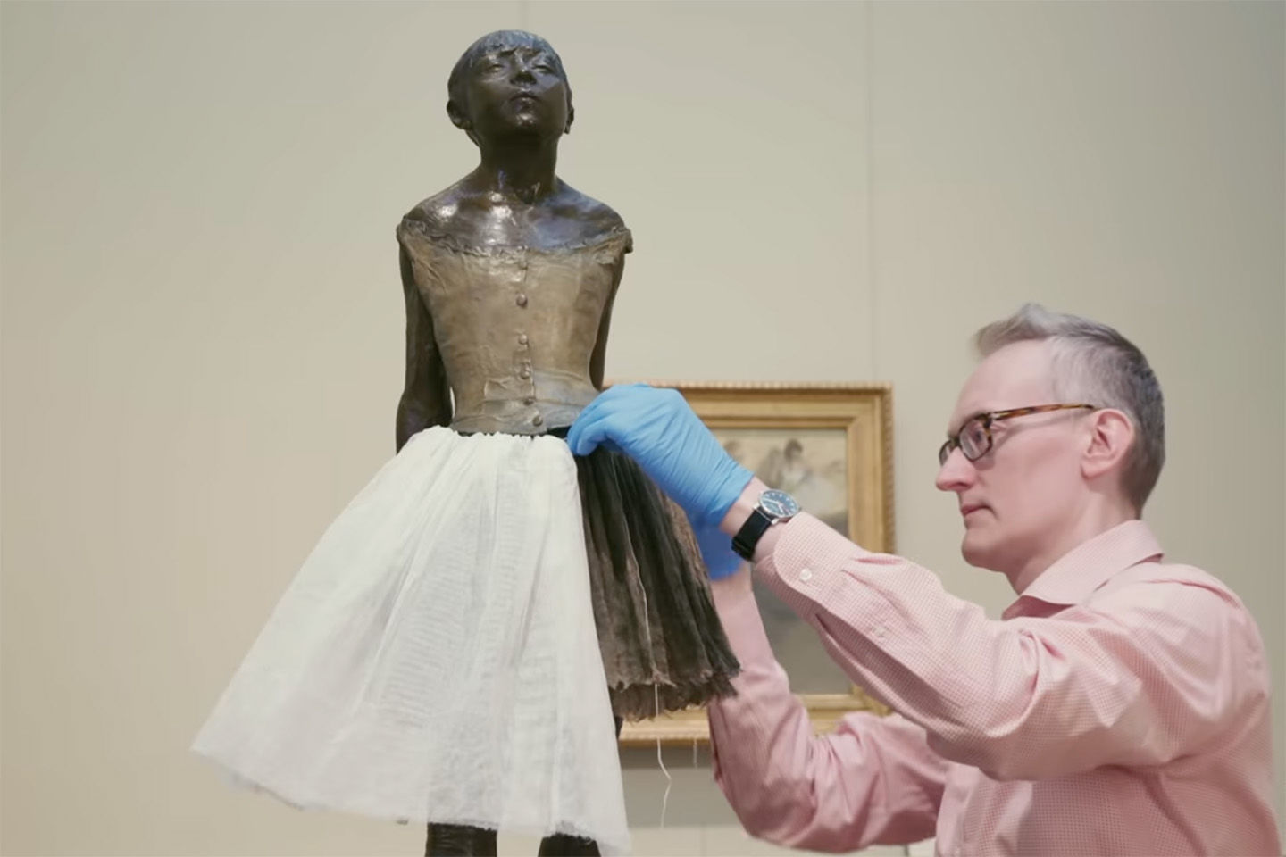 A costume conservator fixes a new tulle skirt to Edgar Degas's sculpture of a young ballerina, 