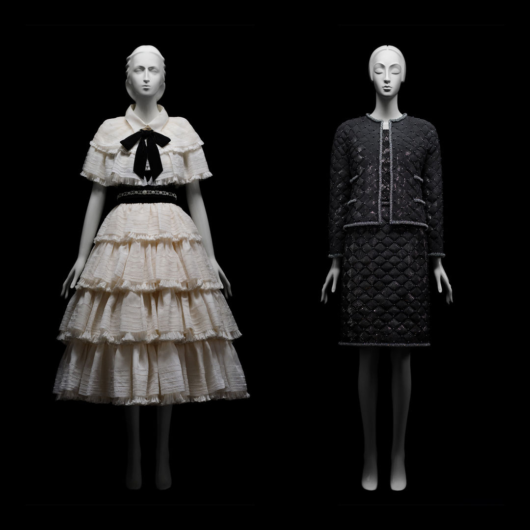 Two Mannequins behind a black background wearing a white dress on the right and a black on the left designed by Karl Lagerfeld. 