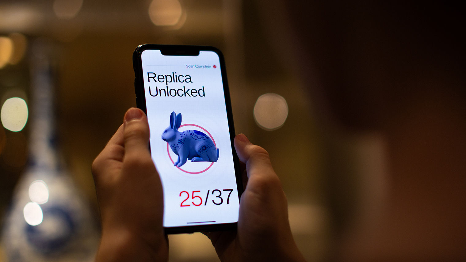 A pair of hands holding a phone and on screen showing a rabbit and the words Replica Unlocked 25/37