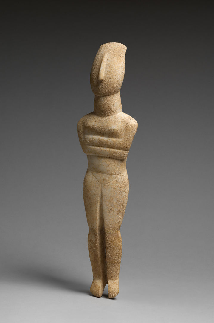 Nude stone Cycladic figure with it's arms crossed. It is against a grey background. 