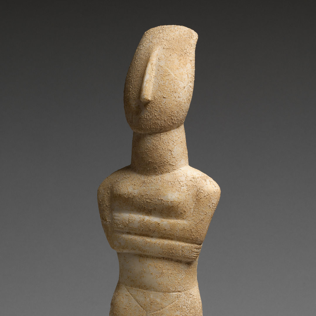 Nude stone Cycladic figure with it's arms crossed against a grey background. 