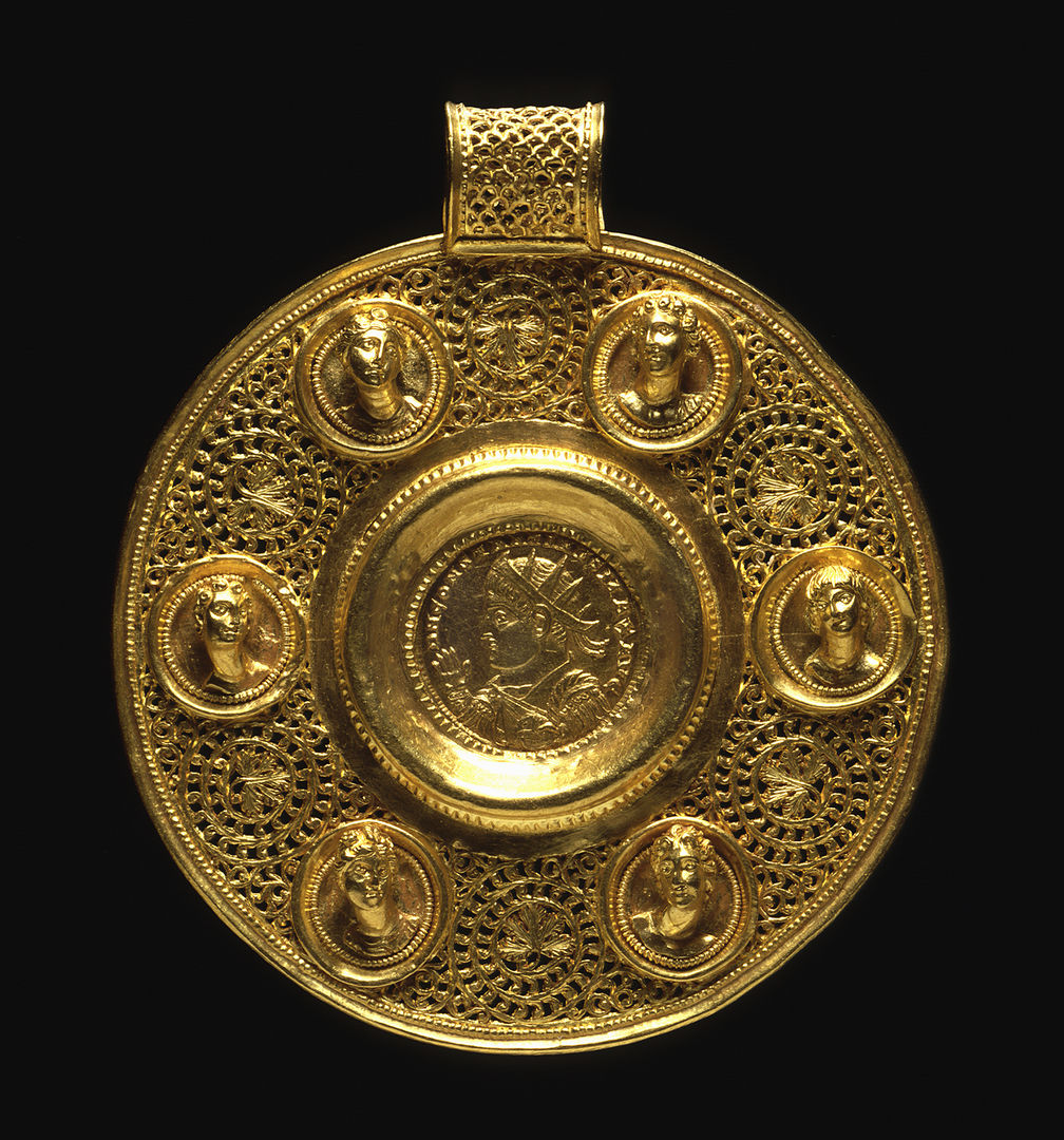 A gold Circular Pendant with Double Solidus of Constantine I with six female reliefs of faces surrounding him coming out of the gold. 