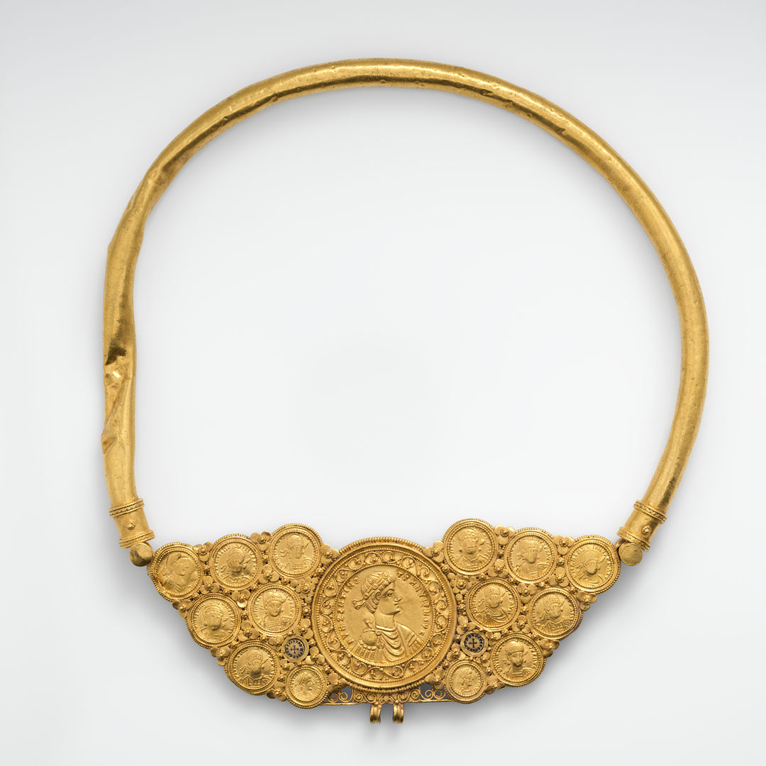 a gold pectoral with coins and a pseudo-medallion that holds fourteen gold coins and two gold discs that are linked together and held by a large gold tube surrounding it. 