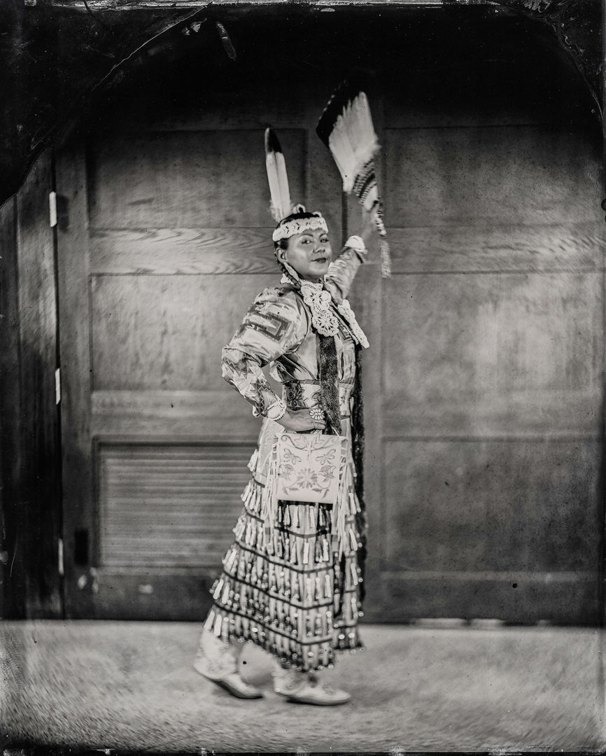 Woman dressed in Native American traditional attire poses and smiles towards the camera
