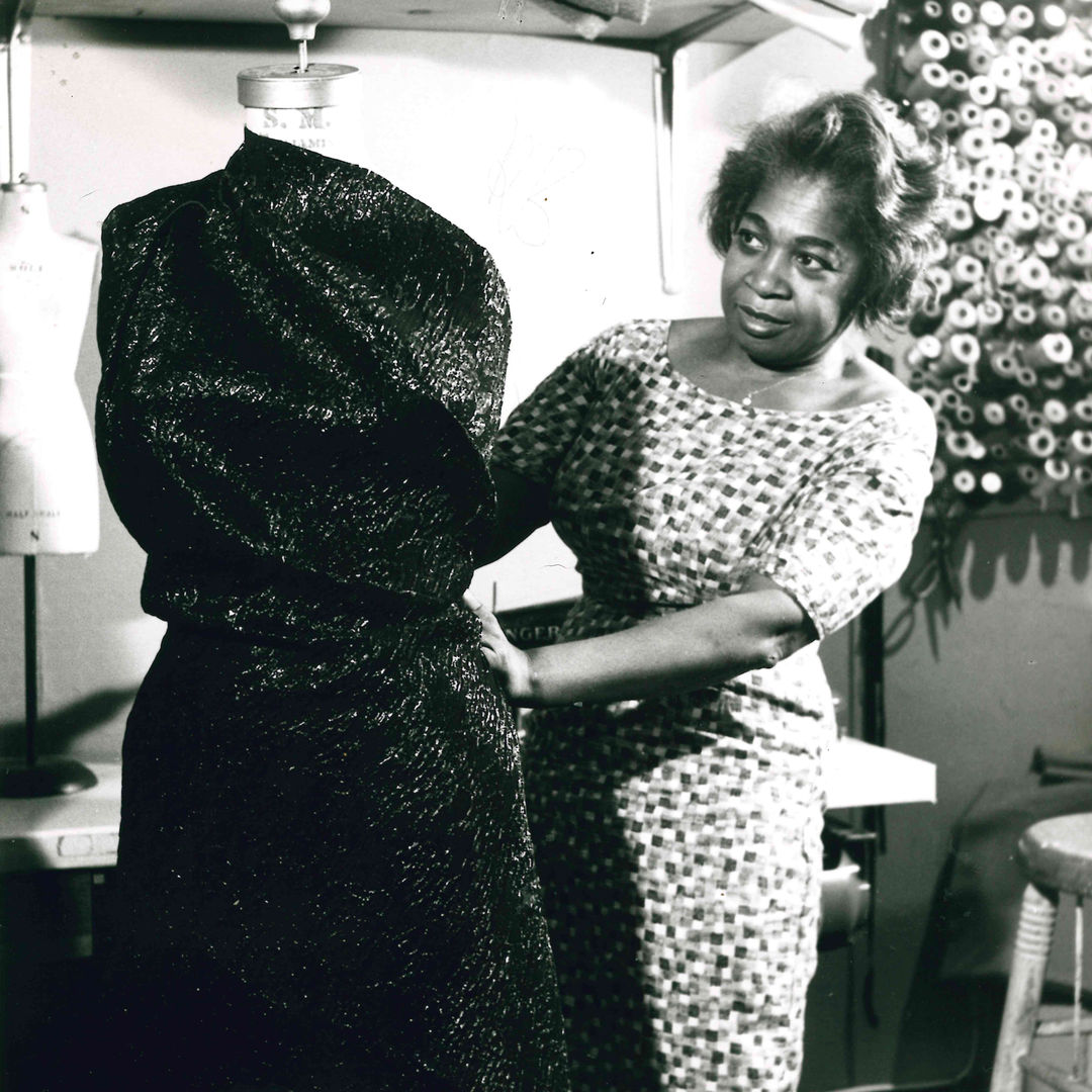 Black and white photo of a woman examining a sequence gown wrapped around a mannequin 