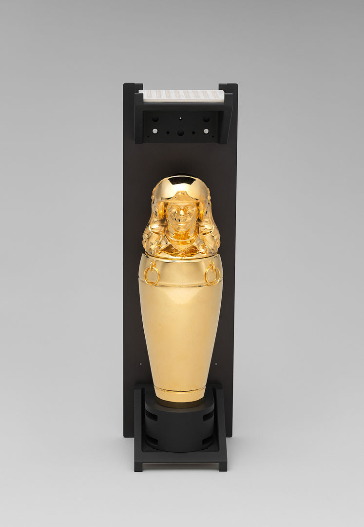 A sleek, shiny golden vessel with a top that looks like an Egyptian statue. 