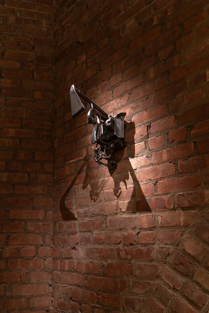 Image of a metal sculpture fused with lots of bits installed onto a red brick wall.