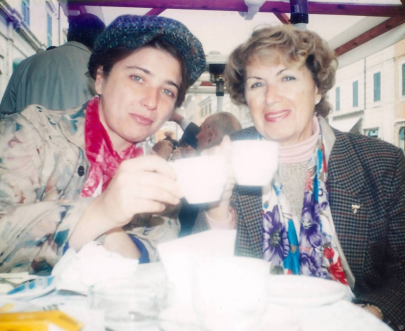 Two women sitting on a table holding up white cups