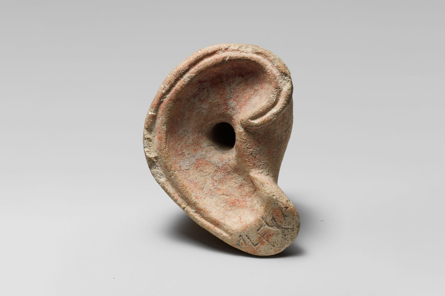 A right ear carved from limestone. Four syllabic signs can be seen on its lobe.