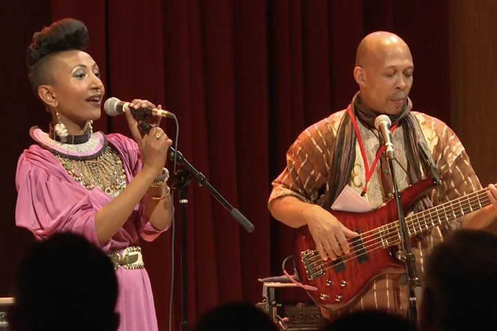 Two members of Alsarah & the Nubatones in performance. The figure on the left is singing, while the figure on the right plays guitar.