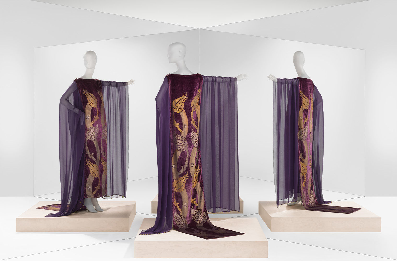 Three mannequins dressed in shoulder to floor purple gown and shawl. 