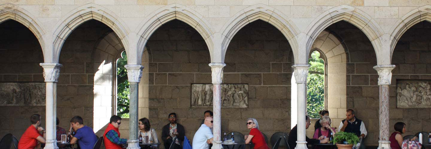 A group of people dine in a cafe situated in a stone medieval cloister.