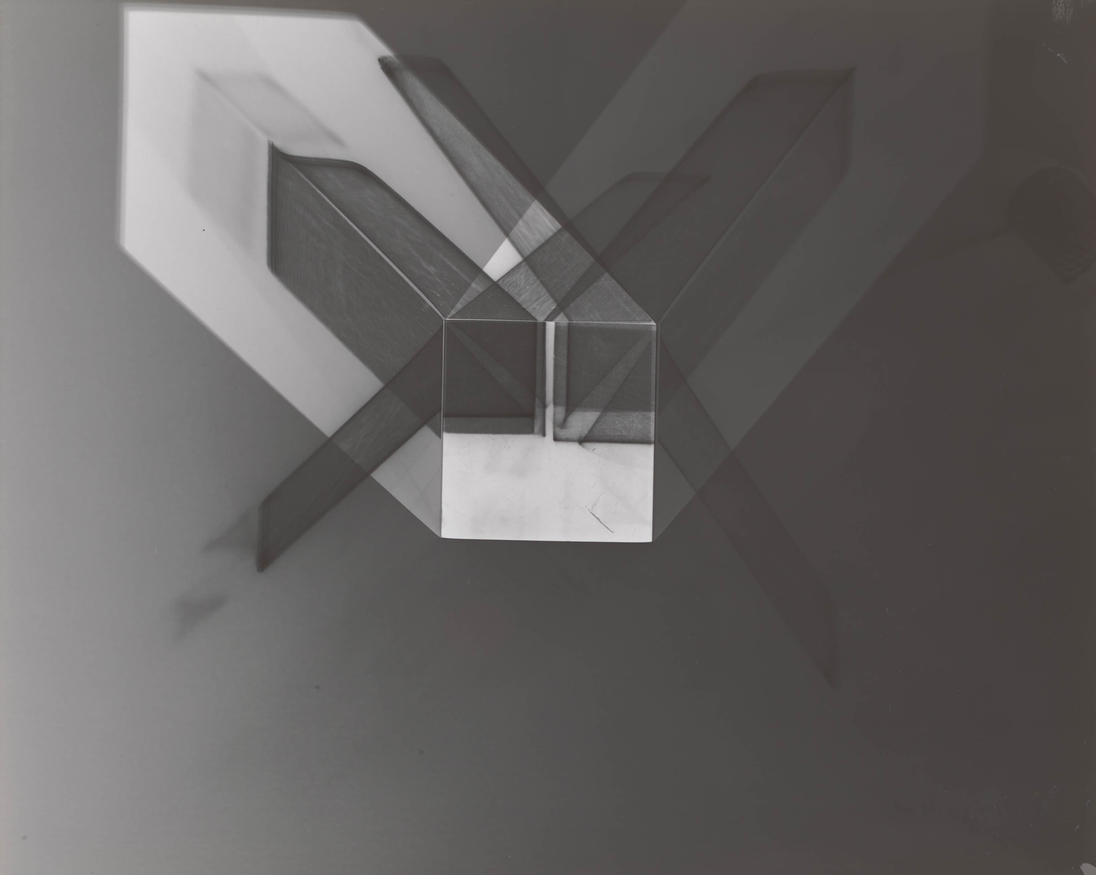 A geometric abstract composition with intersecting translucent shapes, including rectangles and a central cube, creating layered shadows of light on a dark background.