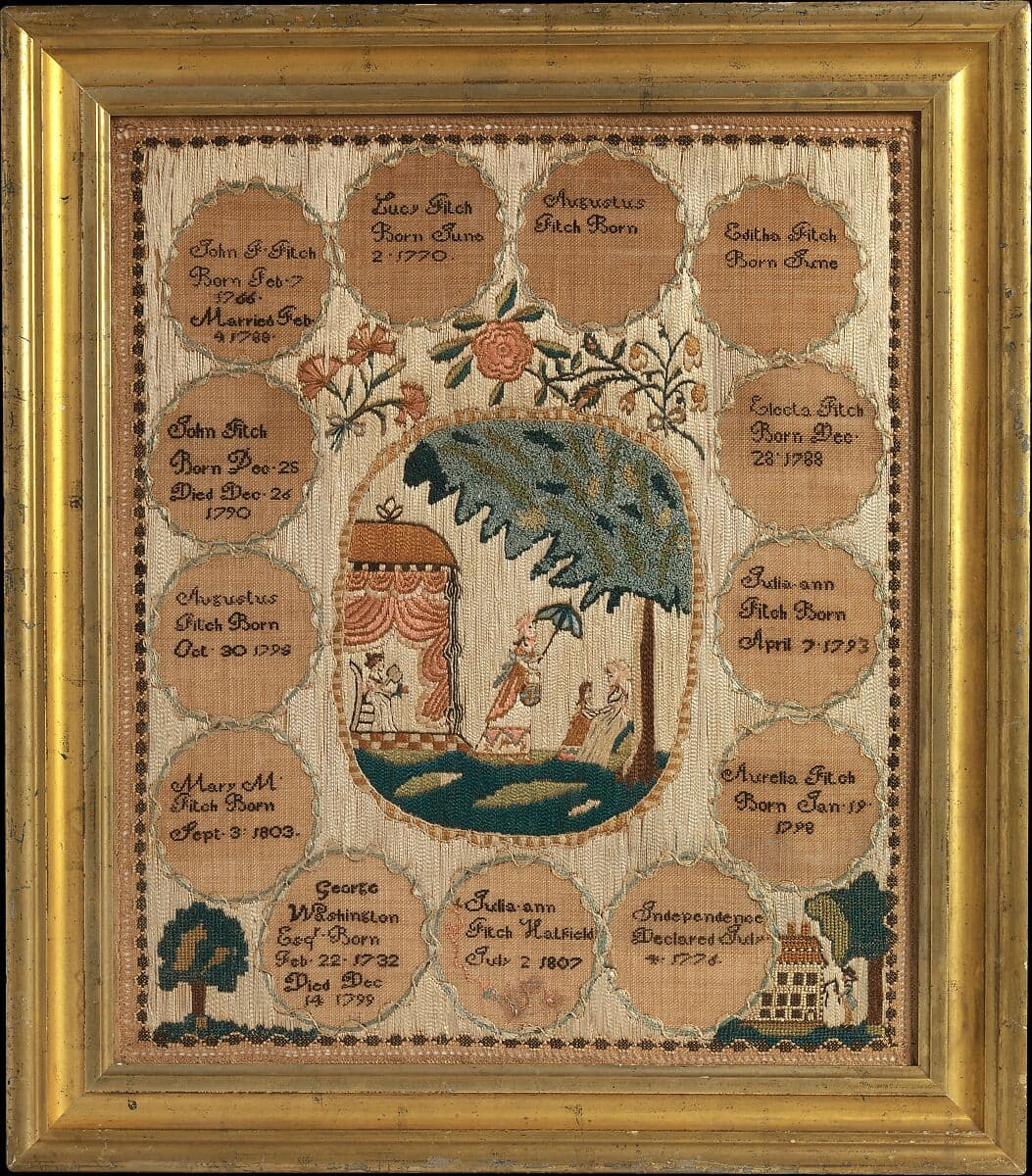 A needlepoint artwork with black text stitched into brown circles around the outer perimeter of the base and surrounding a scene with three women wearing long dresses and a child in an outdoor setting beneath a tree and a pergola covered in pink drapes. One woman walking across grass holds an umbrella. 