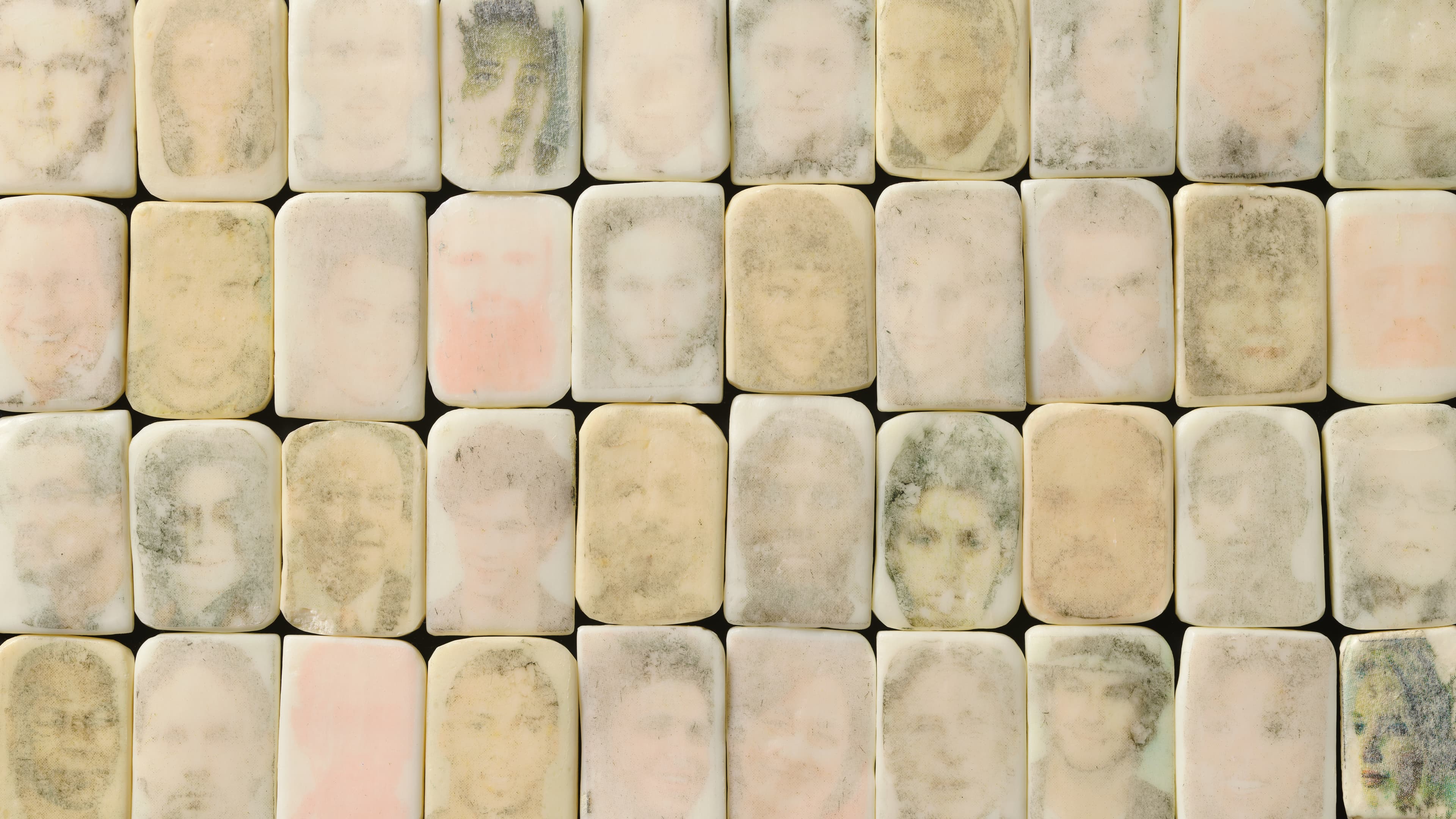 A grid of bars of soap with ghostly images of faces imprinted onto them. 