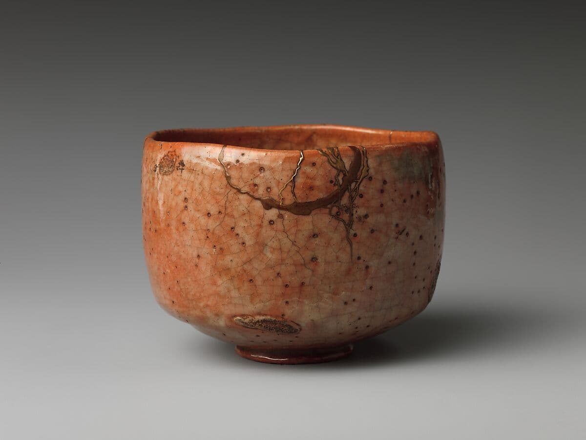 An image of a red stone ware tea cup with a white transparent glaze in places and gold lacquer repairs