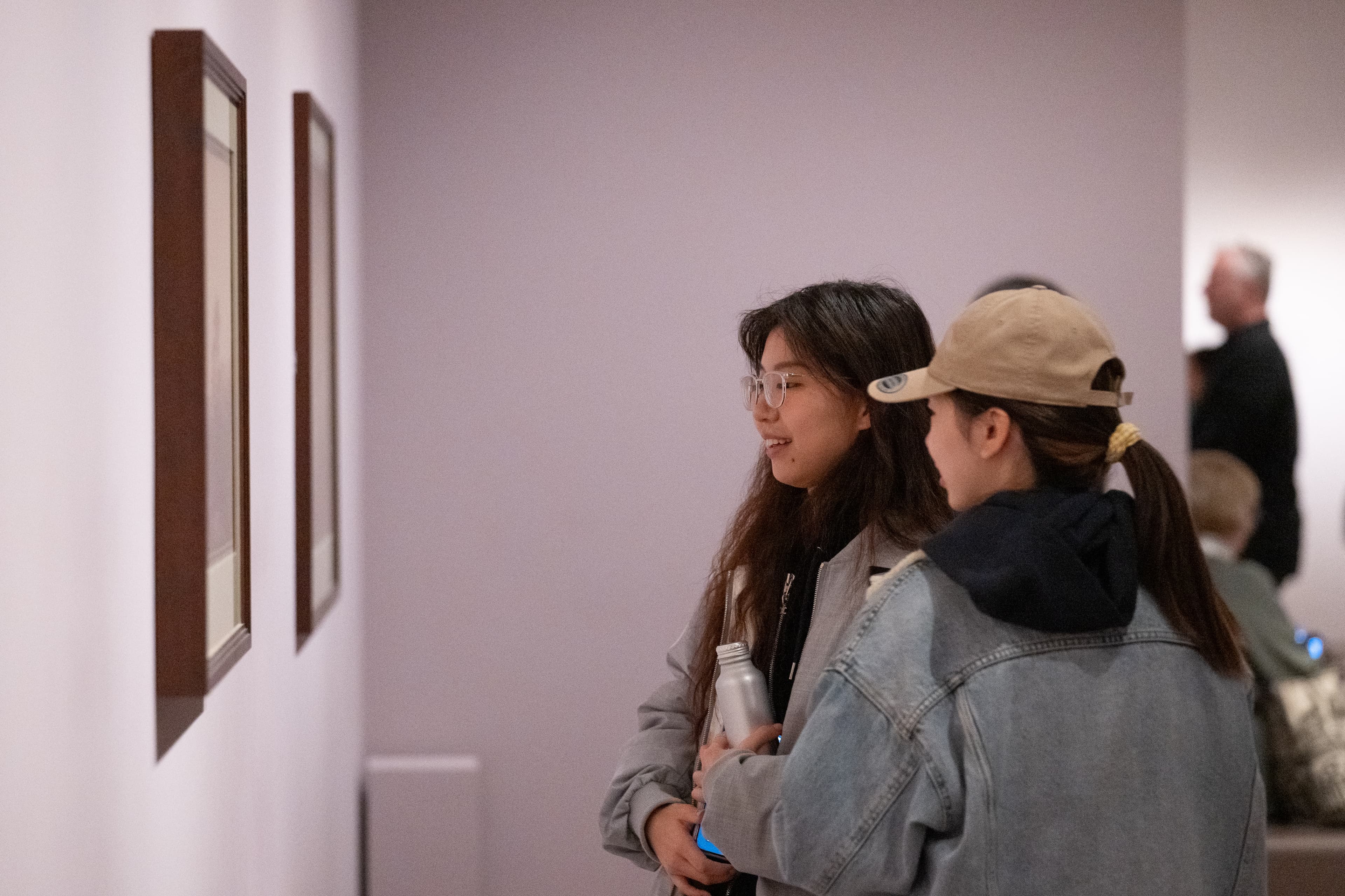 Two Members standing close together looking at a framed artwork.