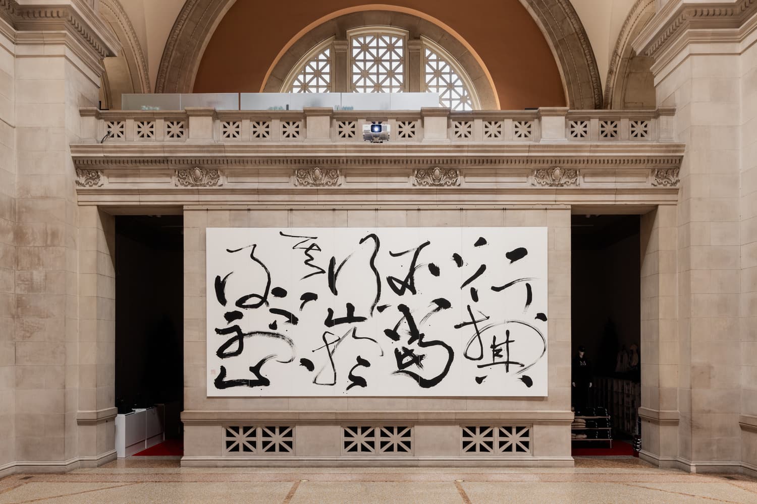 An installation view of Tong Yang-Tze's large scale painting in The Museum’s Great Hall. The painting takes up nearly the entirety of a wall and features expressive strokes of black ink in calligraphic forms on white paper.
