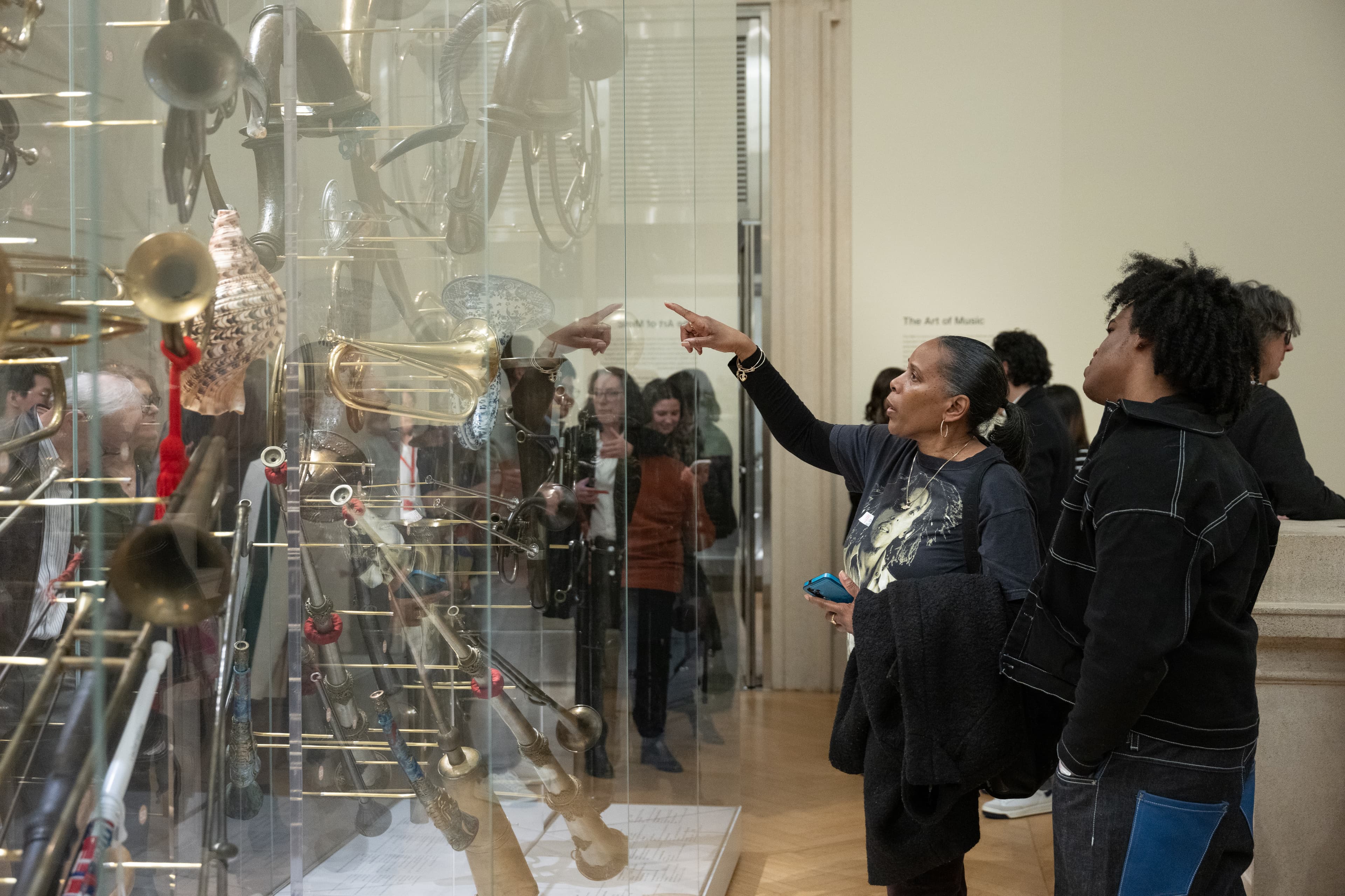Photograph of two teachers pointing and closely examining a glass case of horn musical instruments. 