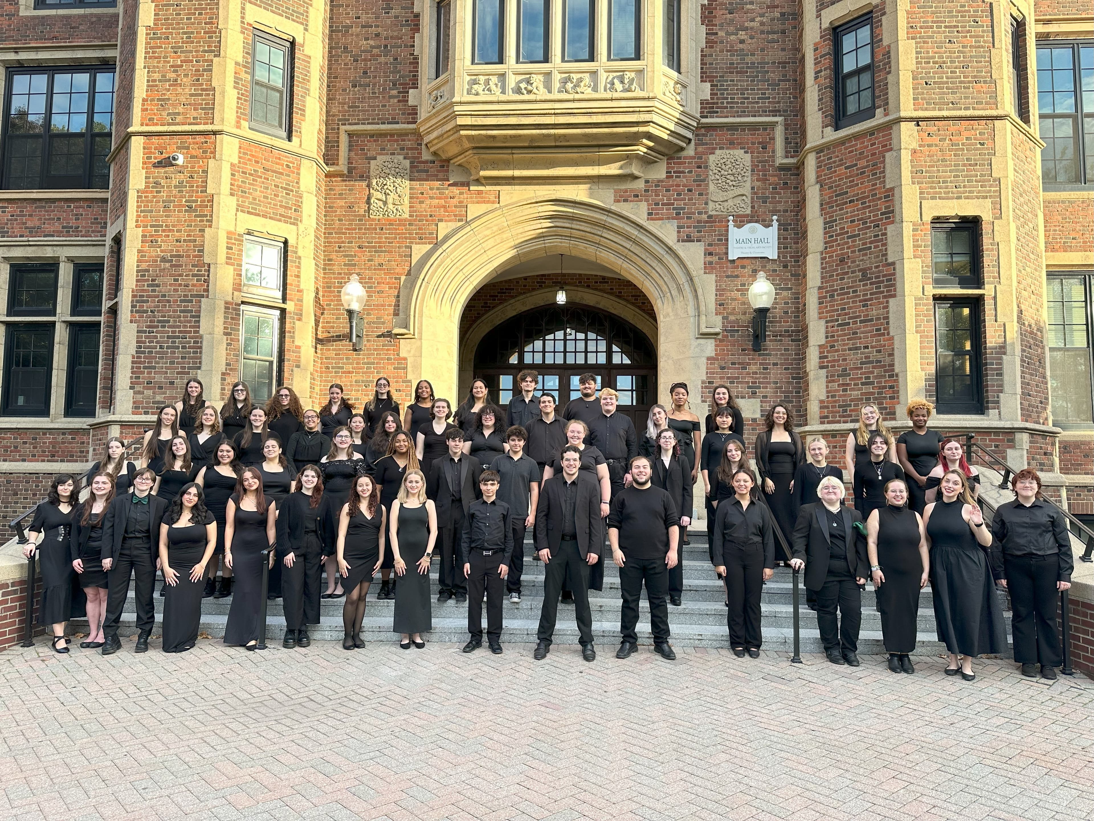 Choir members dressed in black, standing in front of front of a building.