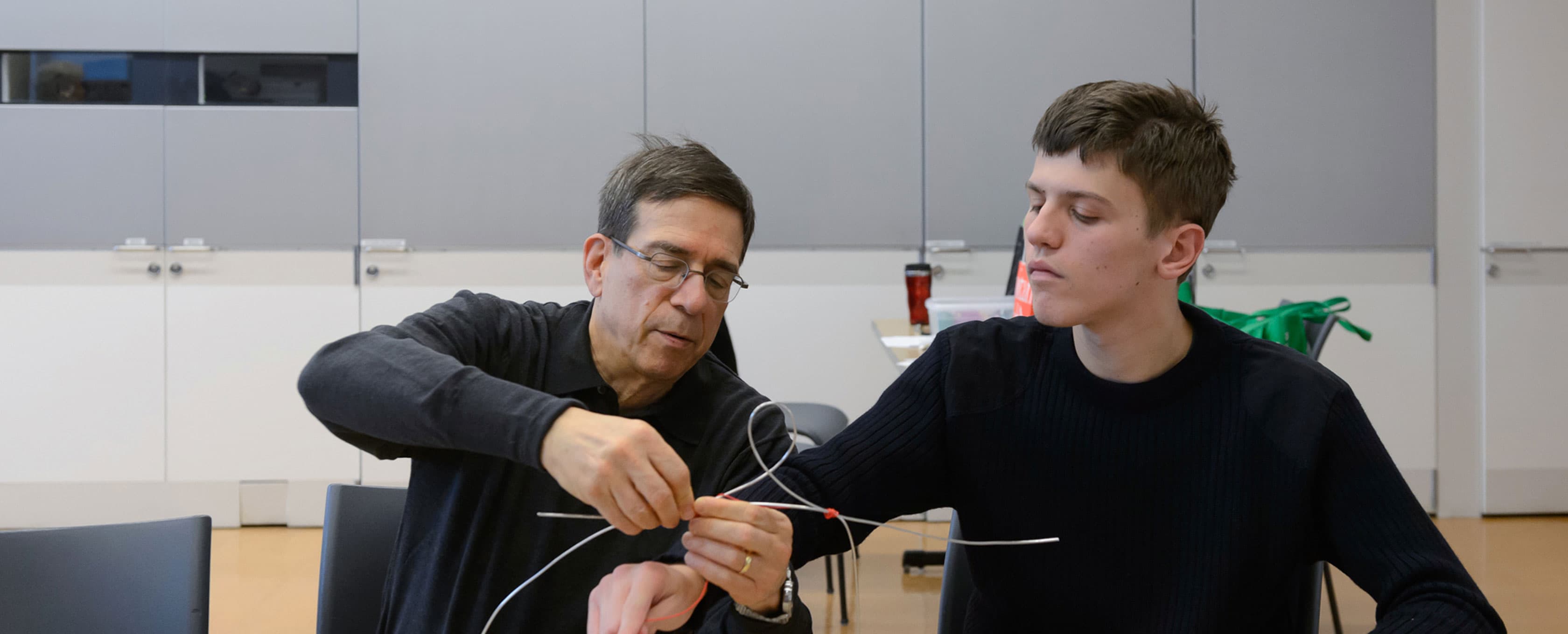 Two visitors sit at a table inside of a studio classroom at The Met. They are working together on a wire sculpture.