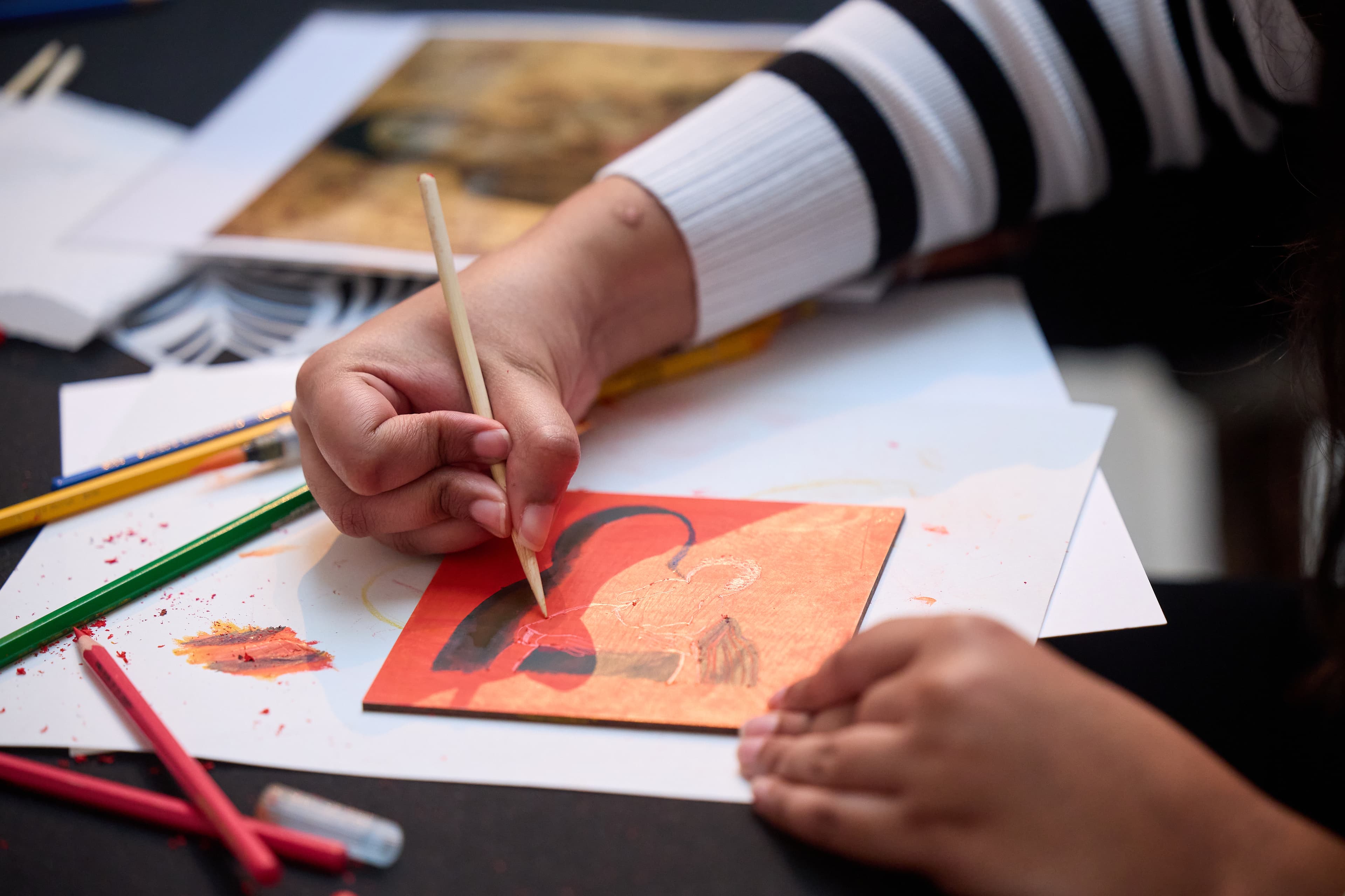 A close up of a workshop participant's hands carving a panel with a wood stylus.