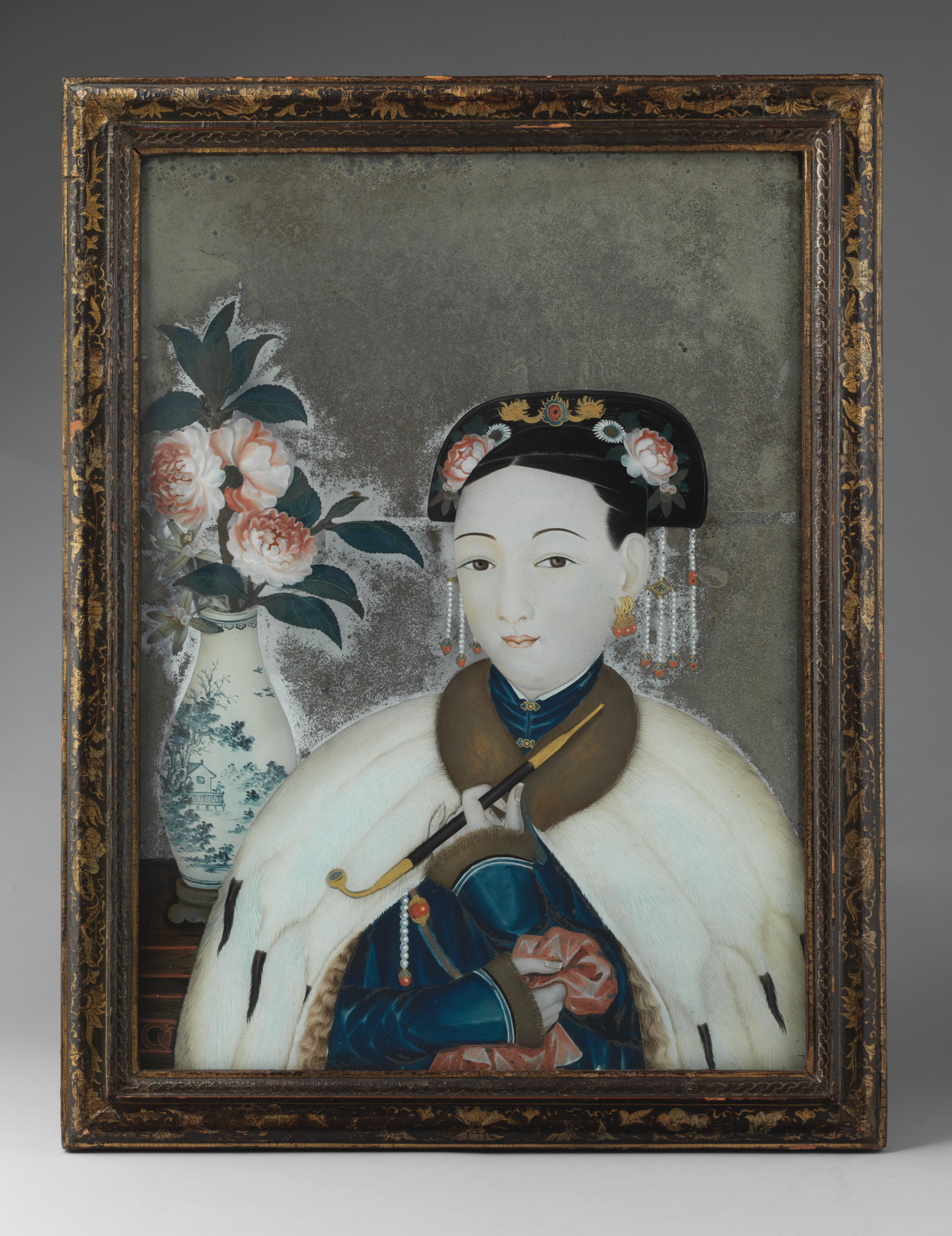 A Chinese woman in furs pauses from smoking her pipe to gaze at the viewer in this seductive reverse-painted mirror decorated in Canton for the European market. This example probably represents a courtesan, who beckons the viewer into a space of fantasy and material desires.