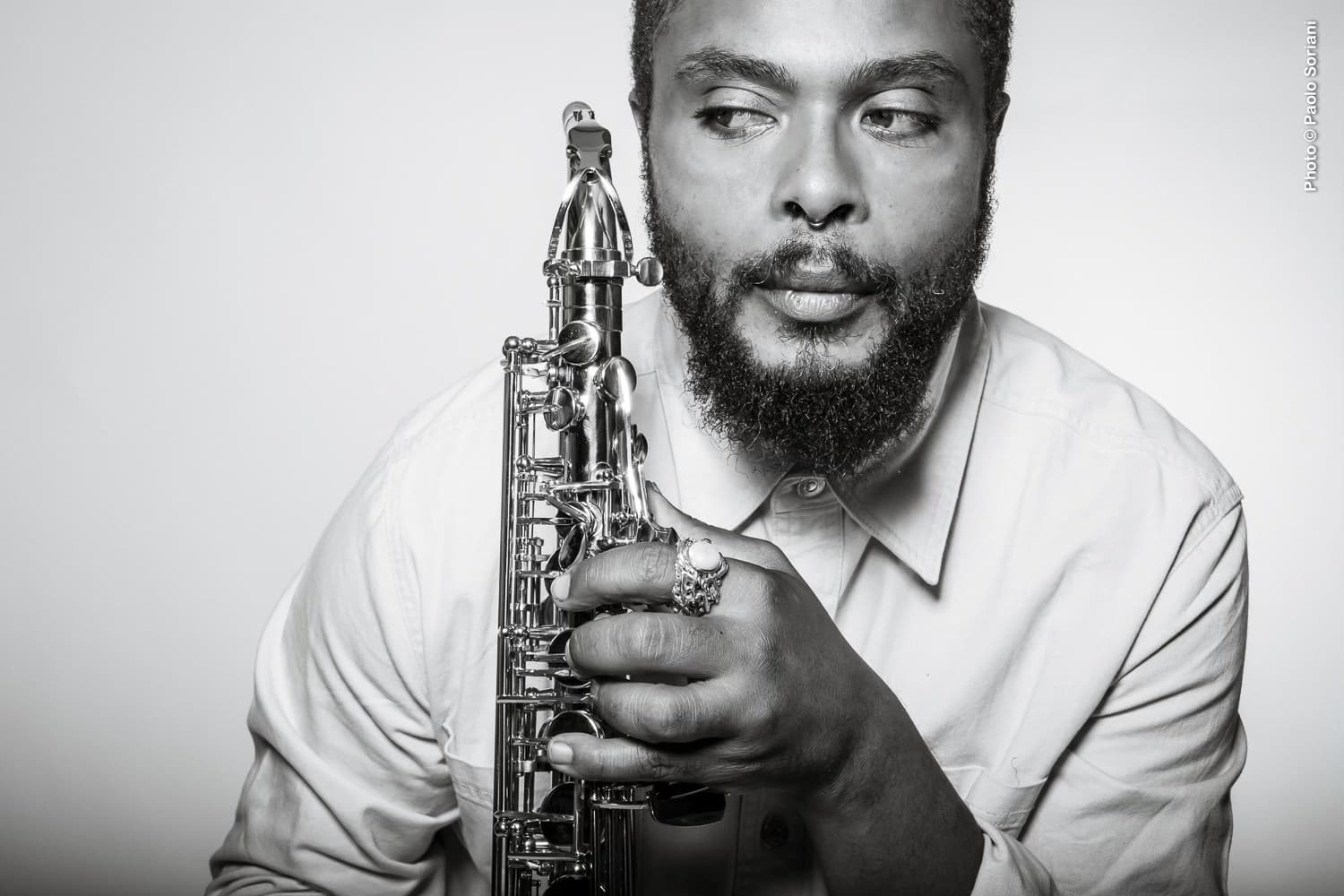 Black and white photo of Logan Richardson holding a saxophone and wearing a long sleeve, buttoned shirt.