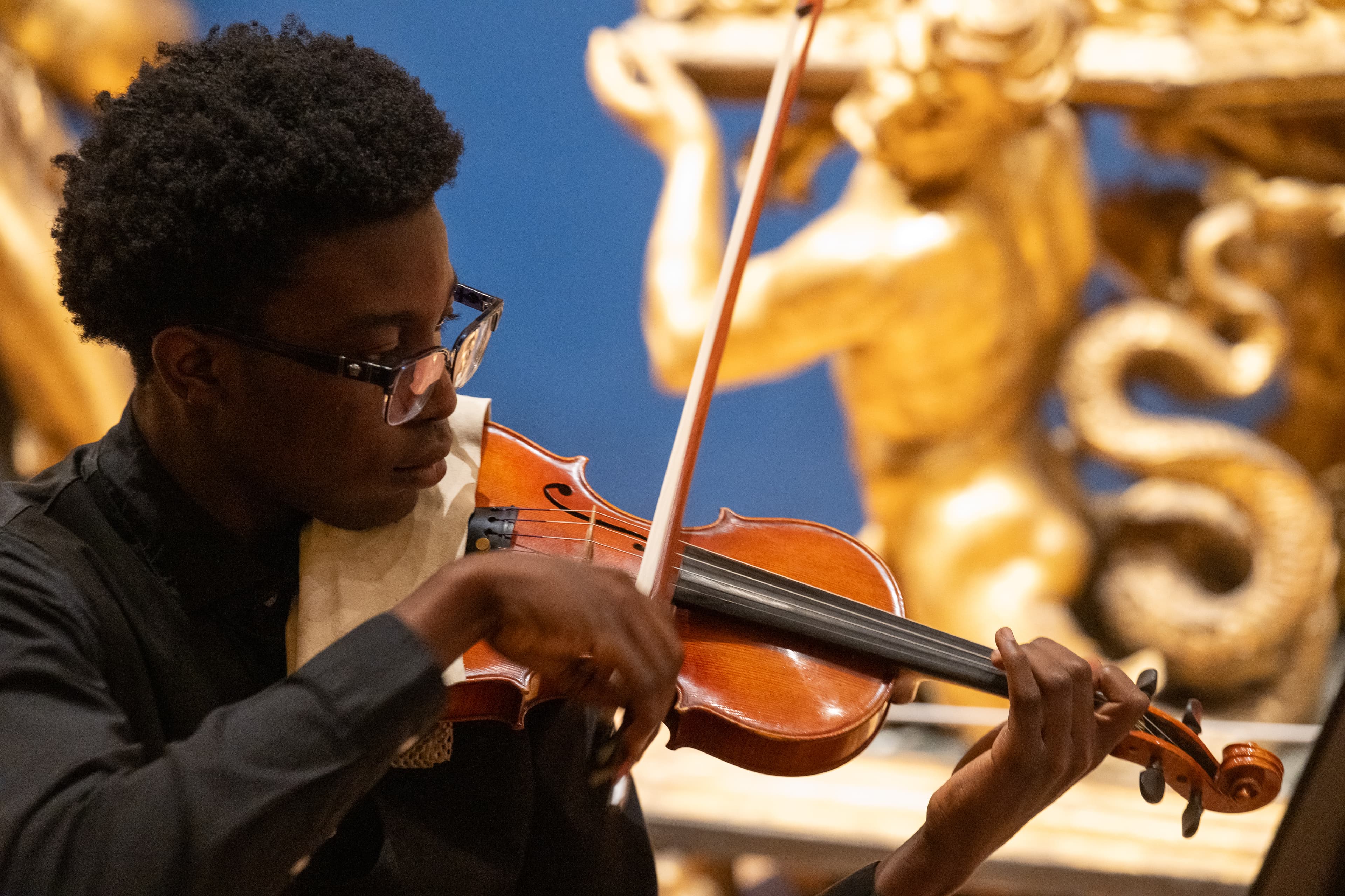 Young musician, wearing glasses and a black shirt playing violin.