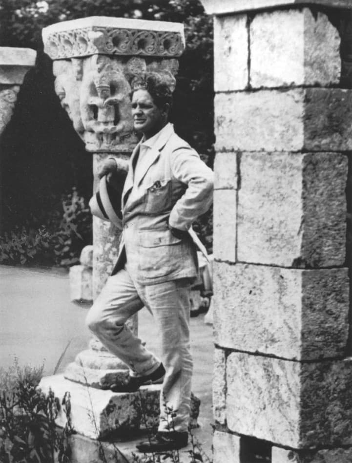 A man standing in from of a medieval column in a black and white photograph