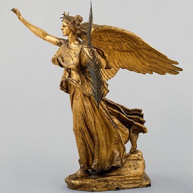 Sculpture of angel facing to the left with hand raised, against grey background