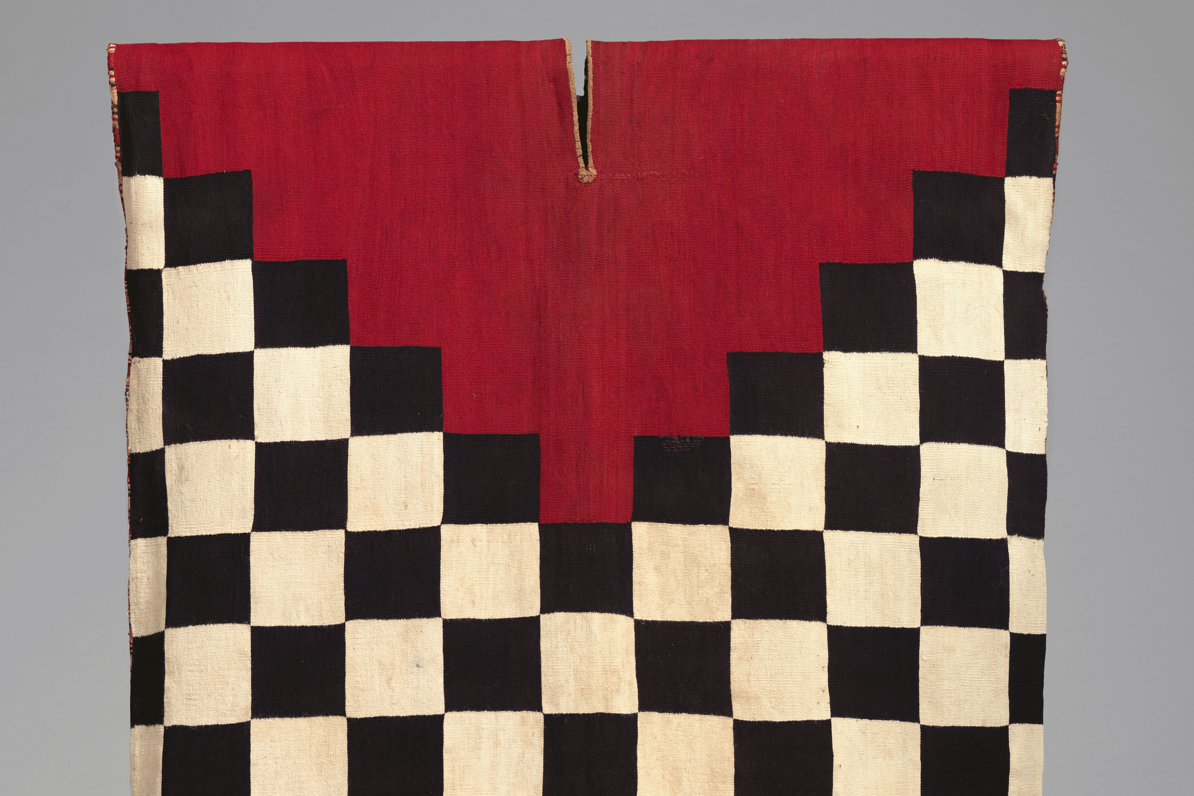 Image shows an Incan tunic, black and white checkered with a triangular red pattern at the top