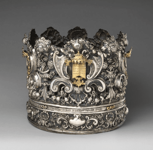 A silver torah crown with intricate detailing and gold highlights.
