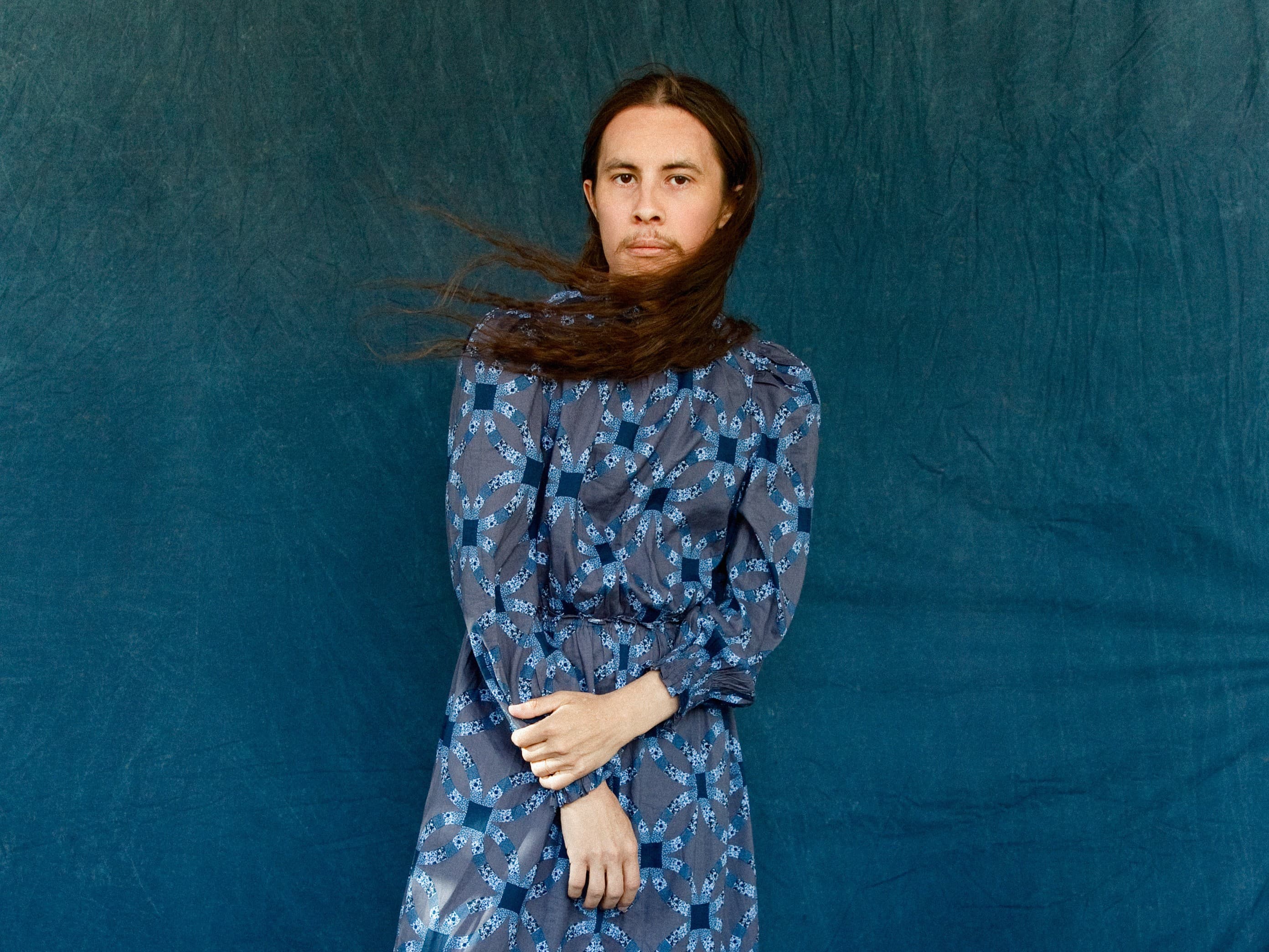 Wyatt C Louis stands facing the camera wearing a blue dress.
