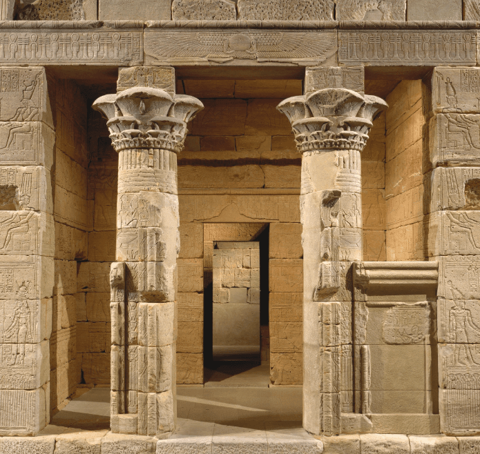 A photograph looking inward towards the Temple of Dendur. Two columns are in the foreground and we see interior rooms behind them with ancient Egyptian reliefs
