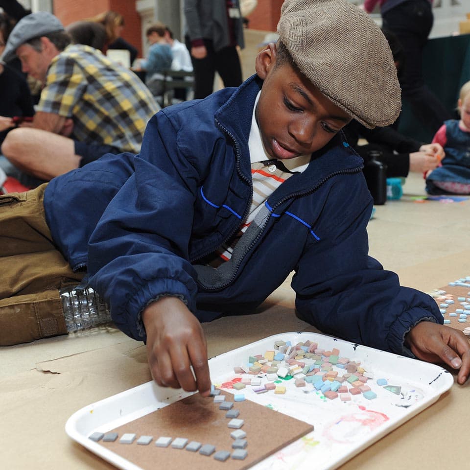 Young children creating mosaic art with small colorful squares on cardboard.
