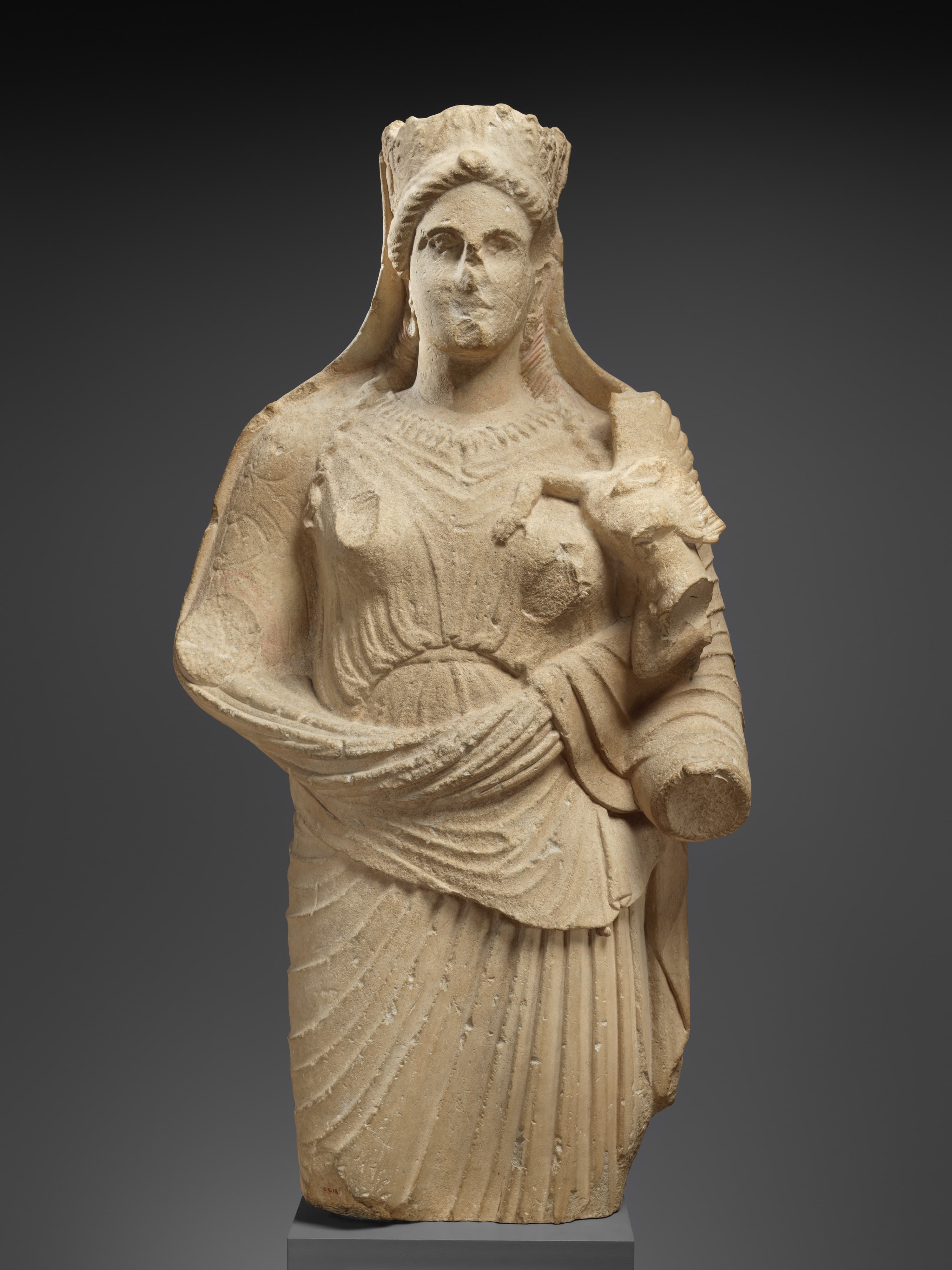 An image of an ancient marble statue of Aphrodite. She is wearing draped clothing and a crown, and is missing her arms.