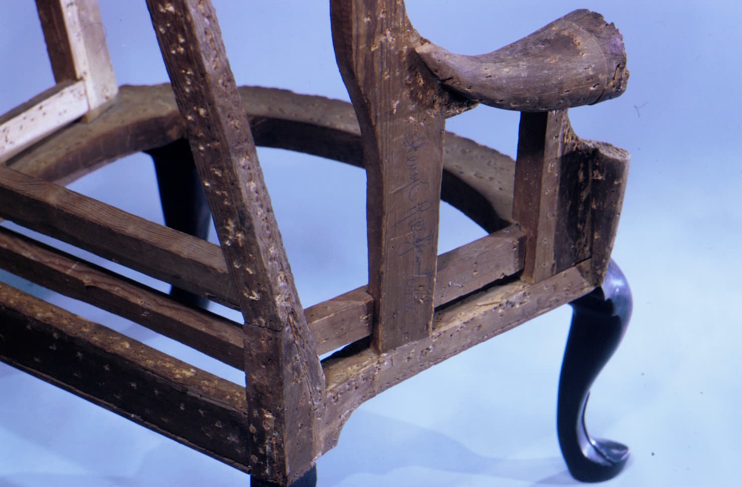 A dynamic angle of a wooden chair. The brown wood of the chairs arm pops from the page against a light blue background.