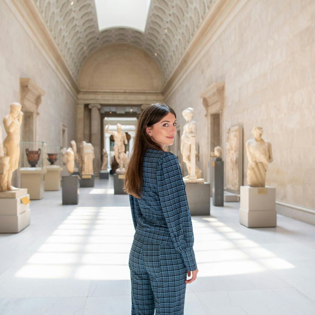 Katy Hessel stands in the sunlit Greek and Roman galleries at The Met Museum.