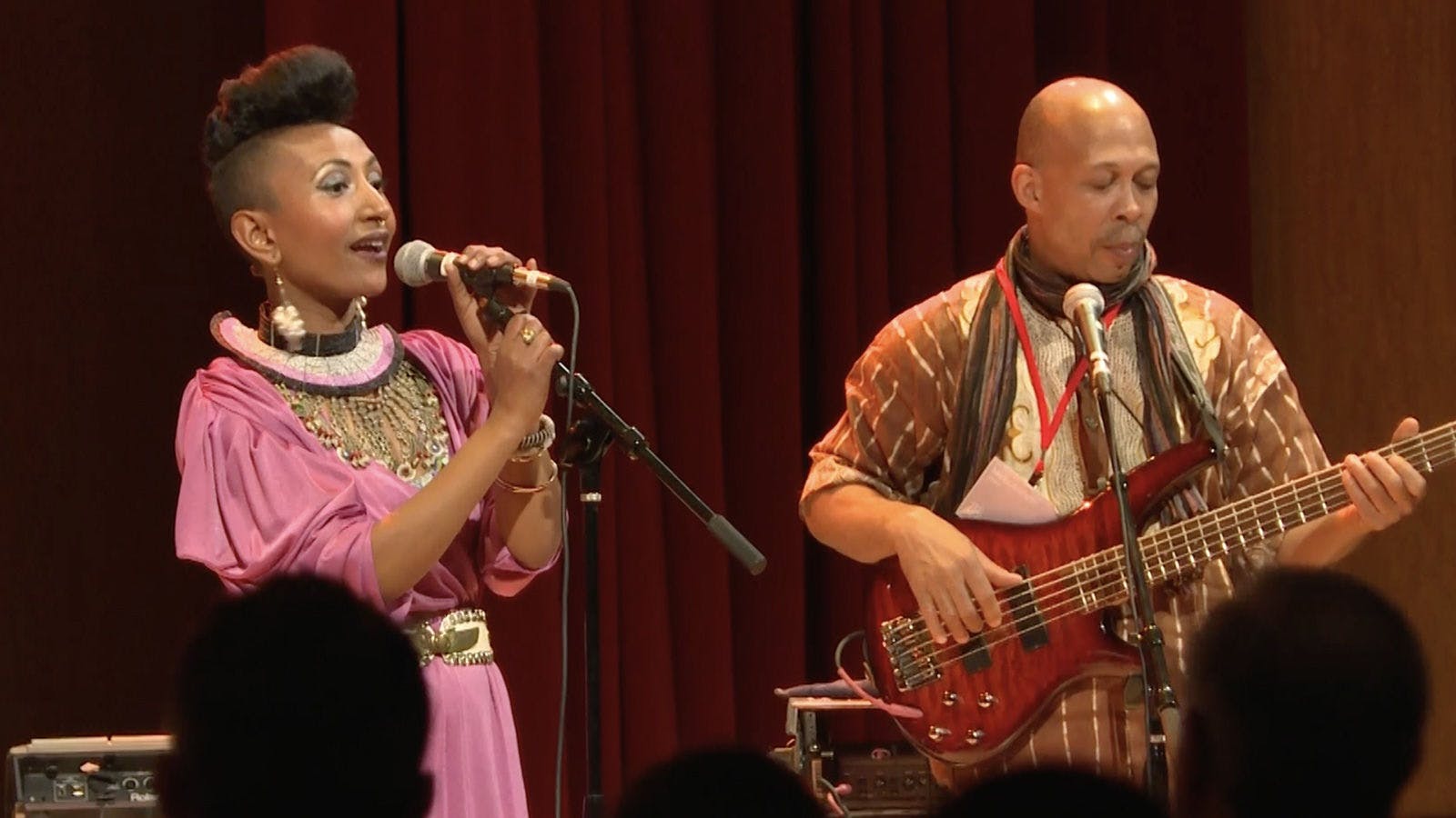 Two members of Alsarah & the Nubatones in performance. The figure on the left is singing, while the figure on the right plays guitar.