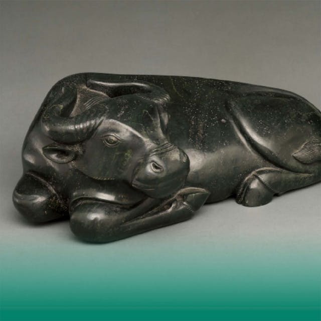 A jade ox lies down with its front legs curled underneath it